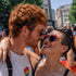 Pride You! | Occhiali da Sole a Cuore Arcobaleno (Love Celebration Special Pick) WYNIE indossati da una coppia uomo e donna che si guardano negli occhi durante una manifestazione del PRIDE, celebrando l'amore e la libertà di esperimersi